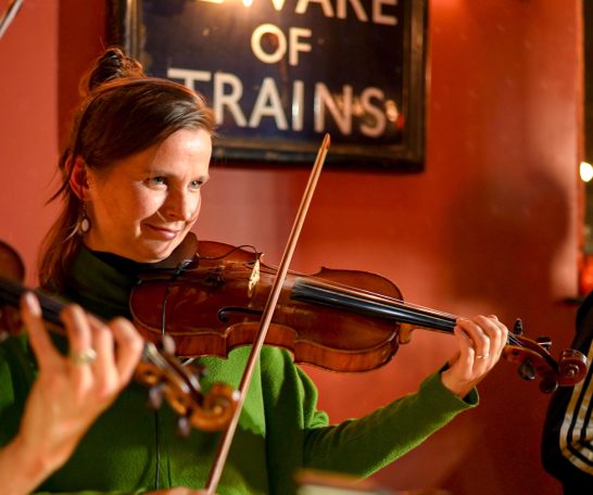 Woman playing the violin, smiling, in a warm, intimate setting.